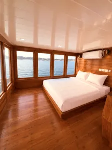 Wooden phinisi stateroom with a double bed and air-conditioning, facing the sea during a shared 3D2N Komodo cruise from Labuan Bajo