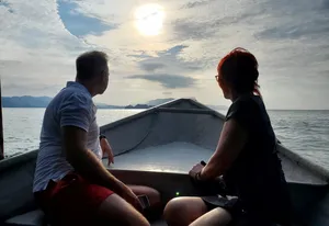 Silhouette of two passengers on a small boat at sunset over the Andaman Sea in Langkawi during a mangrove cruise
