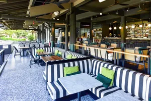 Striped bench seating and arched patio tables beside a well-stocked bar in a Singapore team cooking challenge venue