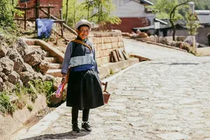Seorang wanita tempatan berpakaian tradisional berdiri di laluan batu di Dali, Yunnan, sambil membawa bekalan dalam perjalanan kereta persendirian