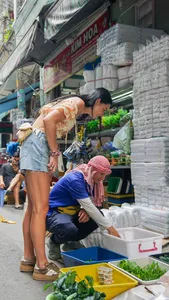一位穿着花上衣的旅行者在胡志明市参加自行车之旅时,浏览街头市集摊位,旁边是装满新鲜香草的托盘