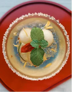 Herbal infusion in a red bowl for TCM mocktails, garnished with mint leaves and sliced roots during workshops in Singapore
