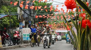 Cyclists and motorbikes cross a decorated Vietnamese street under red bunting flags during a Mekong Island bike tour