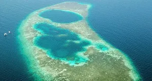 Aerial view of Blue Ring Reef, turquoise reef pools and sandy shallows surrounded by deep blue open water with small boats