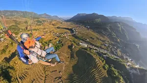 Orange-wing paraglider seated in harness, drifting over zigzag terraced rice plots and mountain slopes with Sapa Paragliding above Sapa