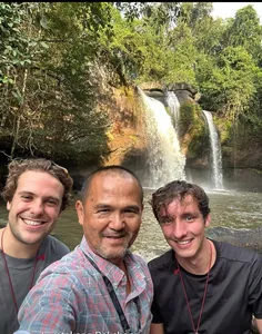 Travellers pose with a local guide beside a waterfall in Khao Yai National Park during a wildlife trek hike
