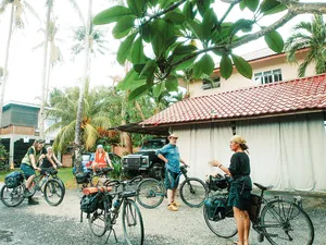 Bicycle Day Langkawi cyclists gather outside a tropical home on Langkawi, with bicycles parked by a red-tiled roof