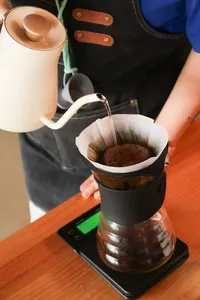 Pour-over coffee brewing: kettle pours into a filter over a dripper stand at a specialty coffee workshop in Lijiang