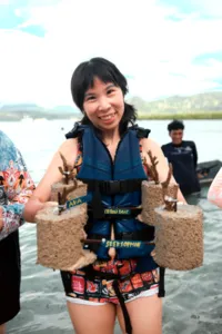 Close-up of a smiling participant holding cement coral plugs in water during coral planting with Rinca Coral Nursery Program in Labuan Bajo