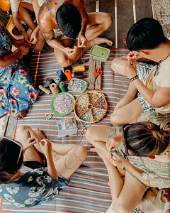 Participants making bead bracelets while seated on a woven mat inside a wooden hut during the 2D1N Surin Island trip