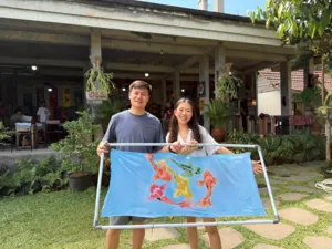 Visitors at Five Arts Studio in Keliki village holding a finished batik cloth outside the artisan courtyard in Bali, Ubud