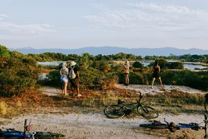 Gravel track cycling in Langkawi: travellers walk with bicycles along the riverbank as bikes rest in the foreground