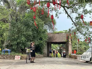 Bicycle rider in a conical hat passing through a gate decorated with red lanterns in Duong Lam ancient village near Hanoi