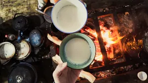 Warm drinks by an open fire, with two ceramic cups offered in a Tibetan family homestay in Shangri-La kitchen