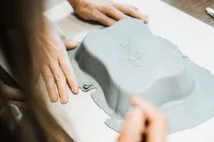 Close-up of hands carving and detailing a grey clay plate with sculpting tools during a Singapore pottery class at the workbench