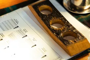 Wooden whisky tasting board with pour wells beside notes on paper in Scotch & Sambal’s hidden home bar in Singapore