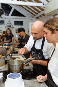 Host in a black apron guides a small group frying and tasting at a Gili T cooking class in Lombok, communal kitchen