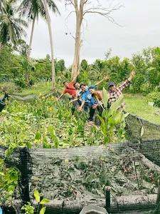 People posing in a Langkawi permaculture vegetable garden at Kebun Lidstari, standing by raised beds of leafy greens
