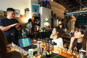 Small-batch whisky tasting in a hidden home bar in Singapore, a host pours for guests at a table of sample glasses and bottles