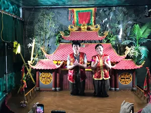 两位身穿红色戏服的第七代水上木偶艺人在河内传统戏台上表演,背景是装饰精美的寺庙风格布景