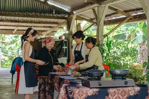 Local family and guests cooking and tasting near a bubbling pot on an outdoor table at an Indigenous Sabahan experience in Kota Kinabalu