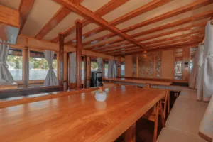On-board lounge on a deluxe phinisi with a long wooden table and bench seating during a 4D3N shared Komodo cruise, Komodo Island