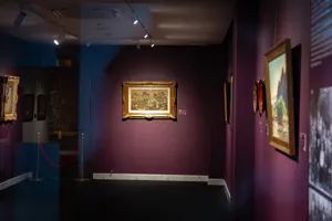 Gallery corridor with framed Vietnamese artworks on purple walls, track lights and rope barrier at Quang San Art Museum in Ho Chi Minh City