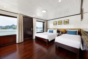 Twin cabin with two beds, blue headboard cushions and large windows showing Halong Bay limestone scenery outside